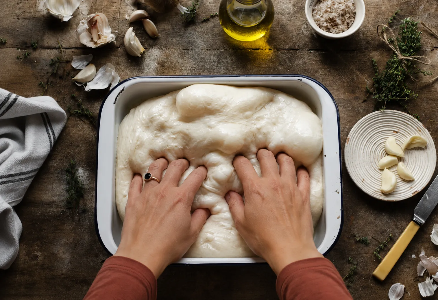 Hände drücken Mulden in einen luftig aufgegangenen Focaccia-Teig